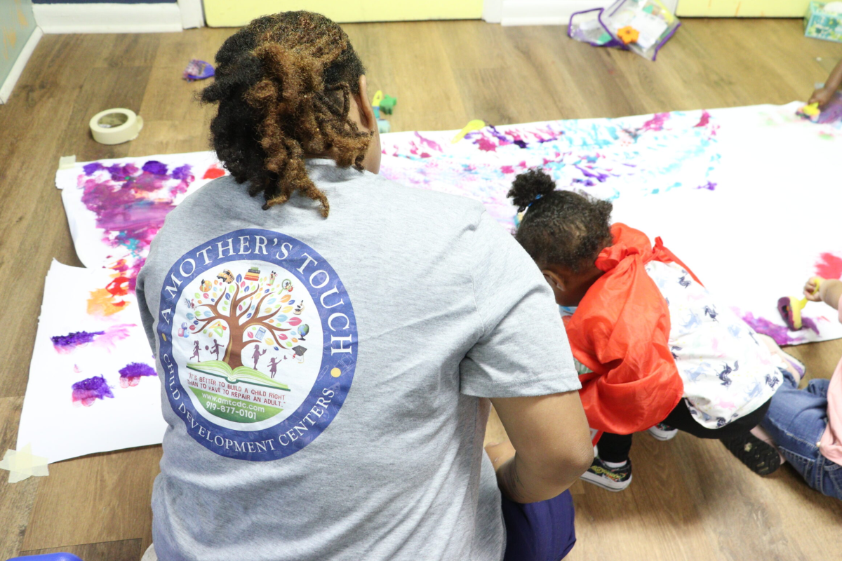 Teacher wearing an A Mother's Touch Child Development Centers shirt doing a finger painting activity with children